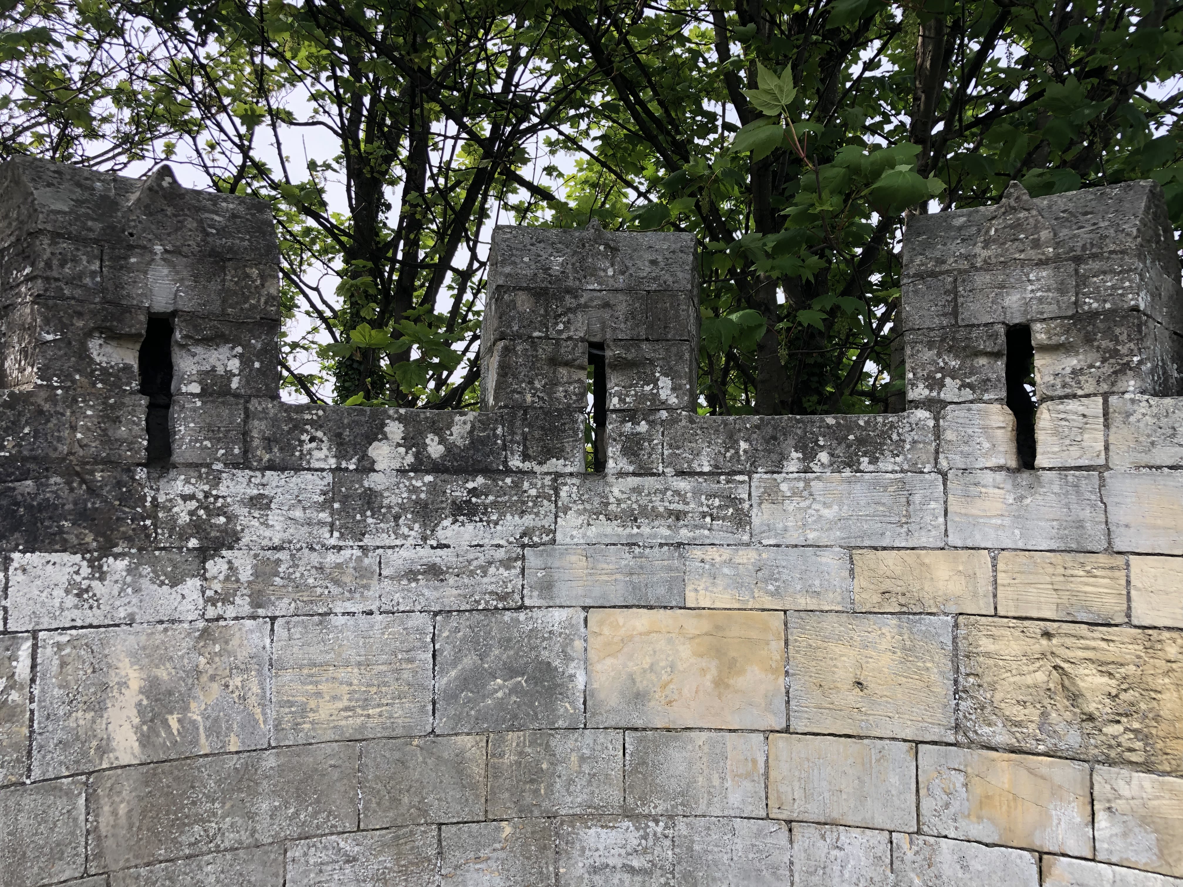 Turrets on a tower of the city walls, with green leaves in the background 