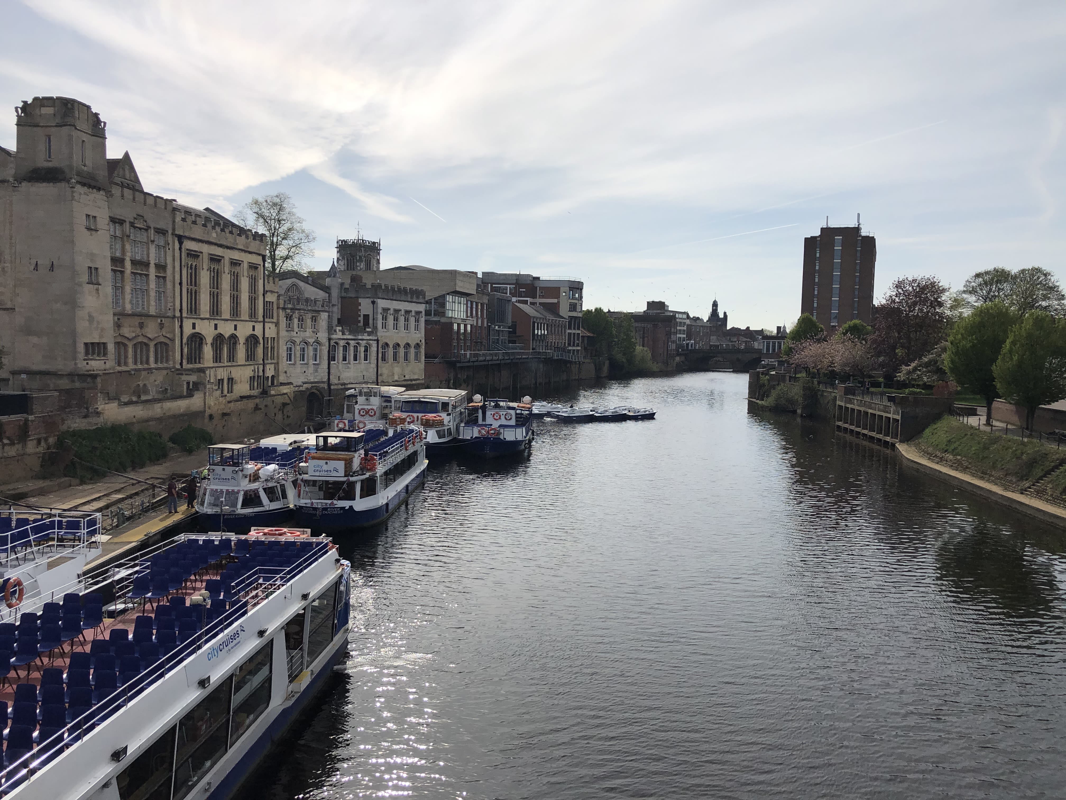 A view of the river with boats, buildings line the shore and a bridge can be seen in the distance